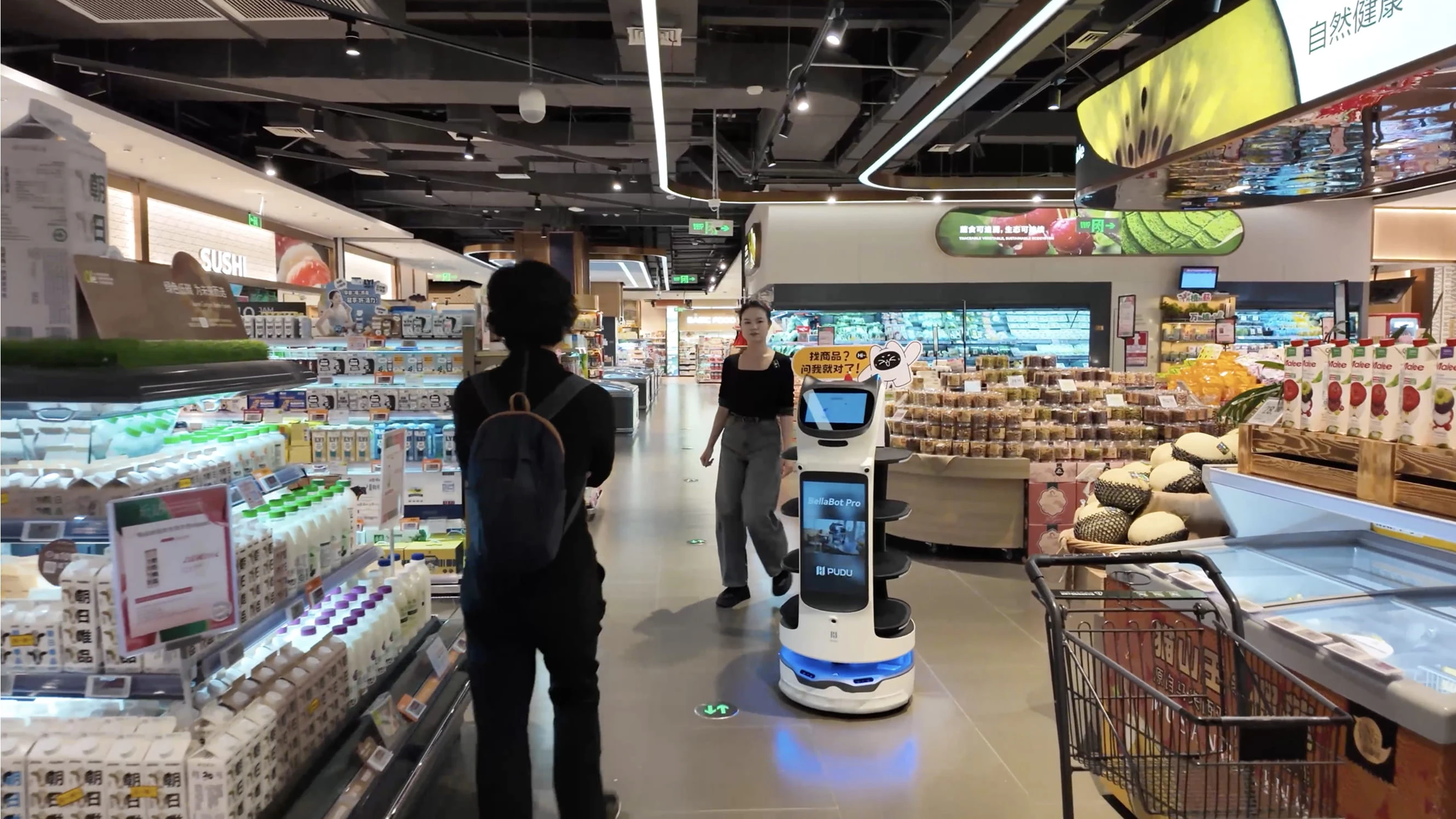 Süpermarket reyonları arasında müşterilerin yanında ilerleyen ekranlı karşılama robotu